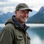 Porträt von Markus Steiner, einem erfahrenen Angelführer, der selbstbewusst in die Kamera lächelt, im Hintergrund sind die Schweizer Alpen zu sehen.